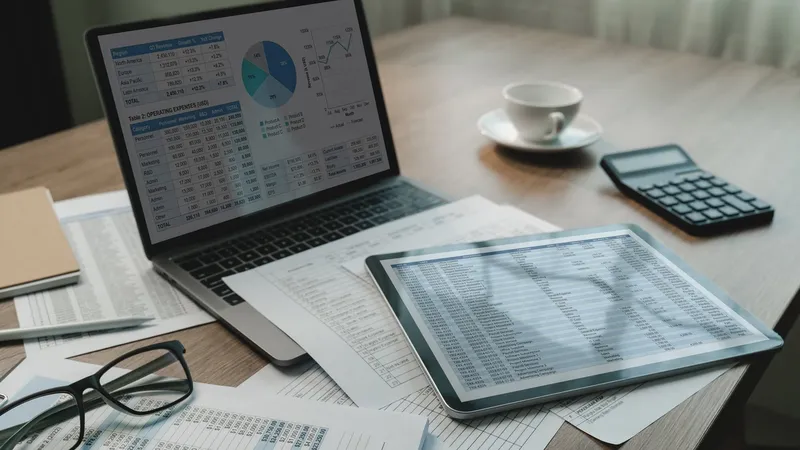 Laptop and tablet showing financial spreadsheets and charts next to a calculator